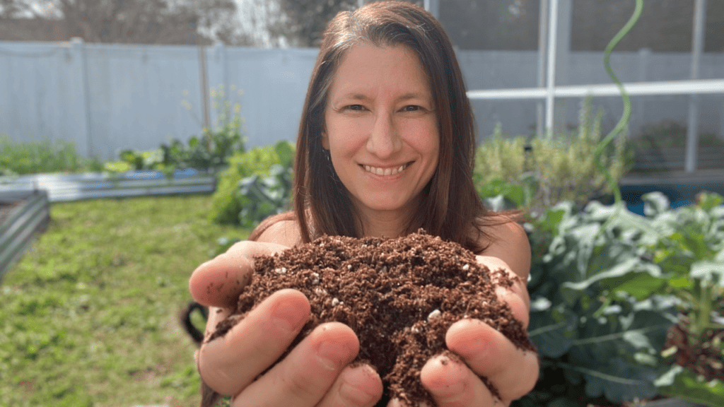 A woman holding up a hand full of rich dark soil used to mix to reuse old potting soil