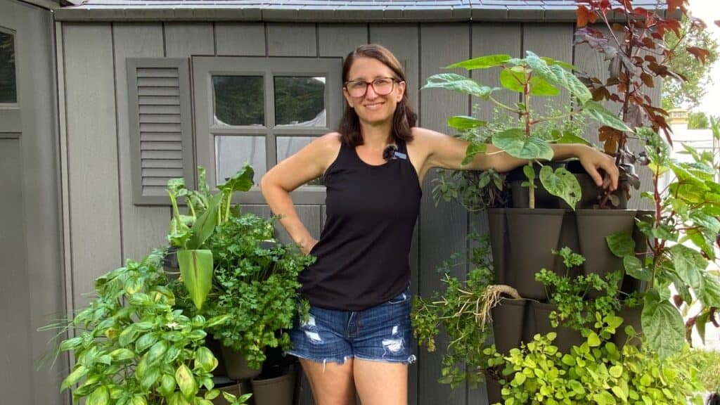 Woman leaning on a vertical planting container with lots of plants growing from it