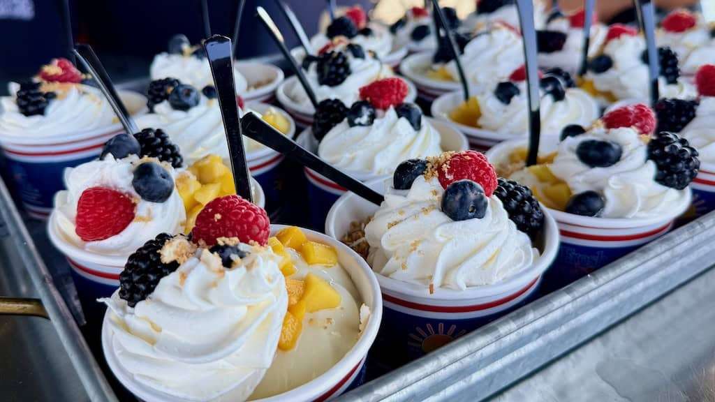 Tray of dessert cups of custard and cream topped with berries and mangos